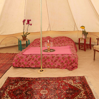 Photo de l'intérieur d"une grande tente avec un grand lit deux personnes et un plateau de dégustation de vins