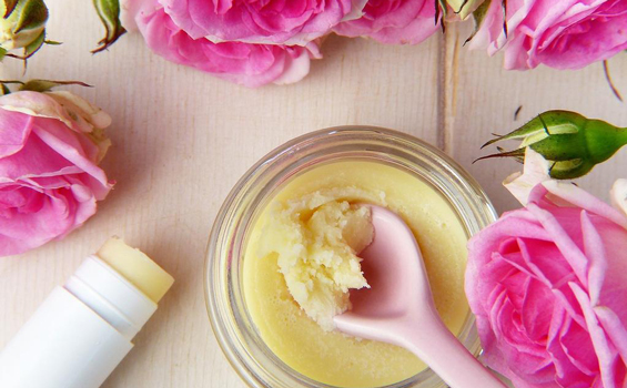 photo vue du dessus d'un baume cosmétique fait maison avec une cuillère en bois entouré de roses