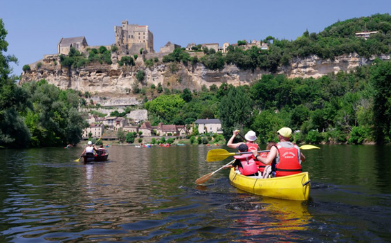 photo des falaises troglodytes au dessus de la Dordogne avec des touristes en canoe